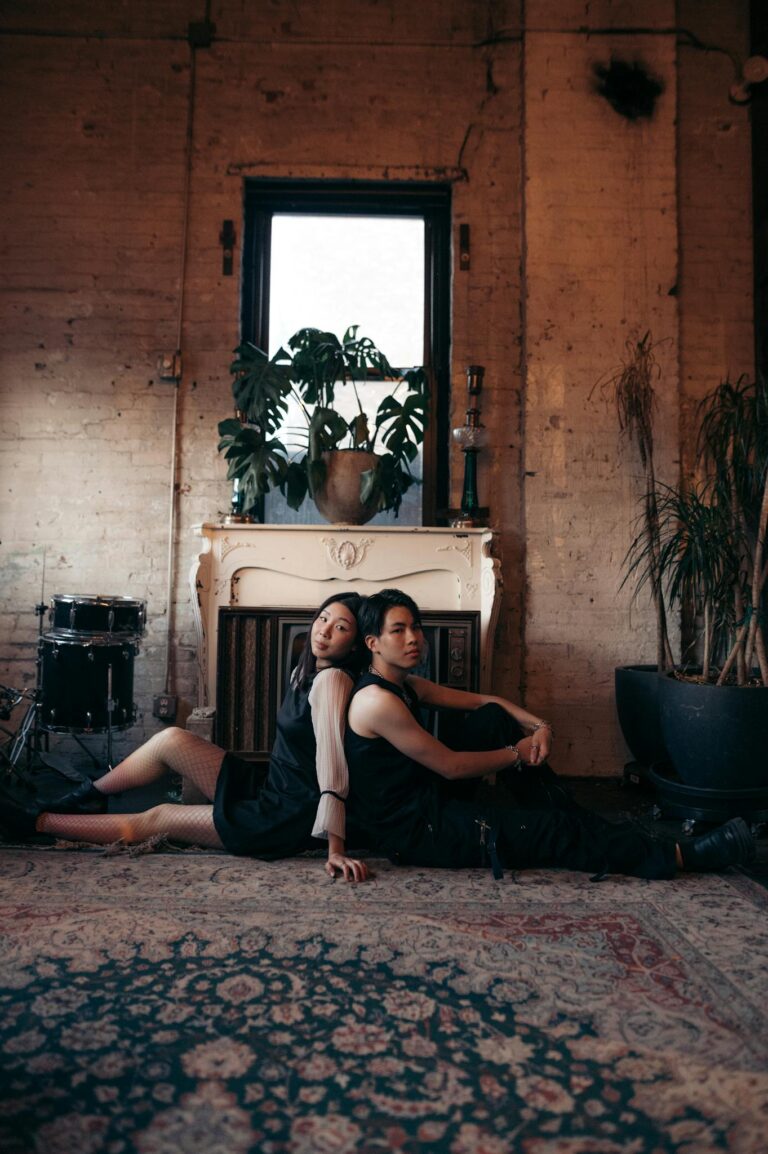 Couple sitting back to back in a stylish indoor setting with plants and percussion instruments.